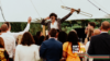 A white man holds a trumpet in the air in front of an energetic crowd facing him