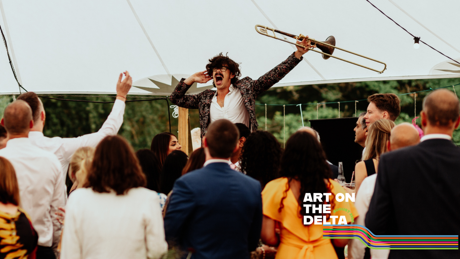 A white man holds a trumpet in the air in front of an energetic crowd facing him
